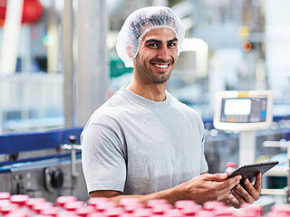 A worker in a factory holding a tablet and smiling to the camera